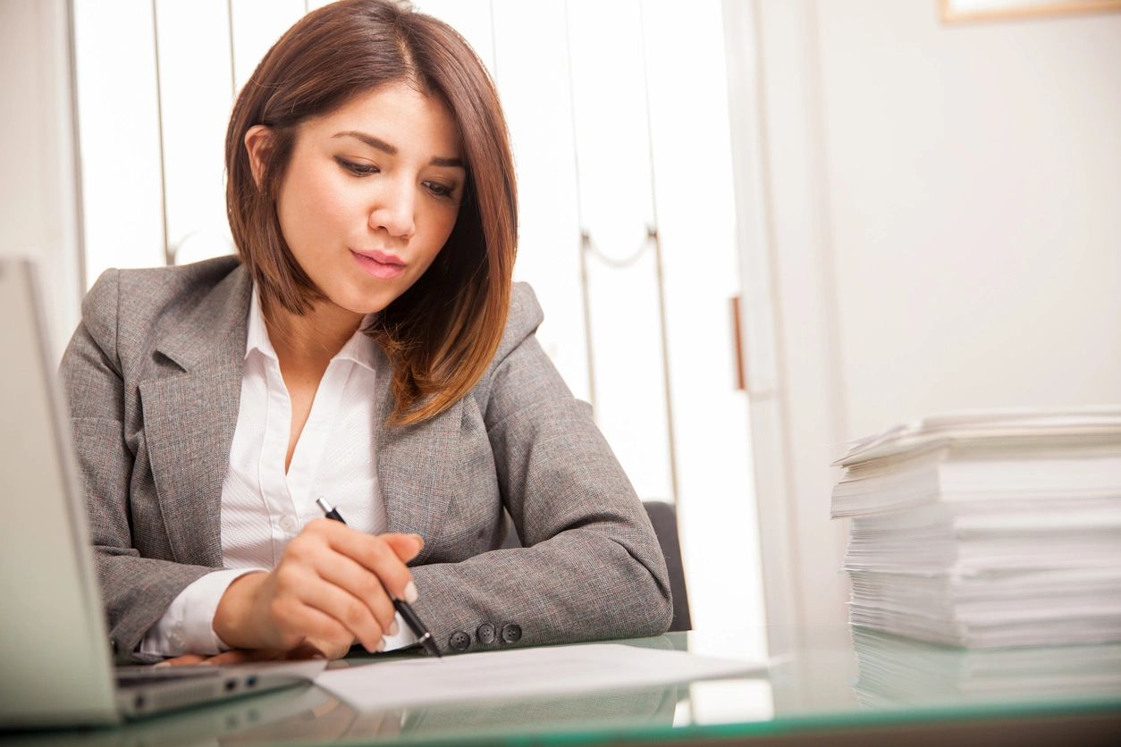 Beautiful young lawyer reviewing and signing a lot of documents at work